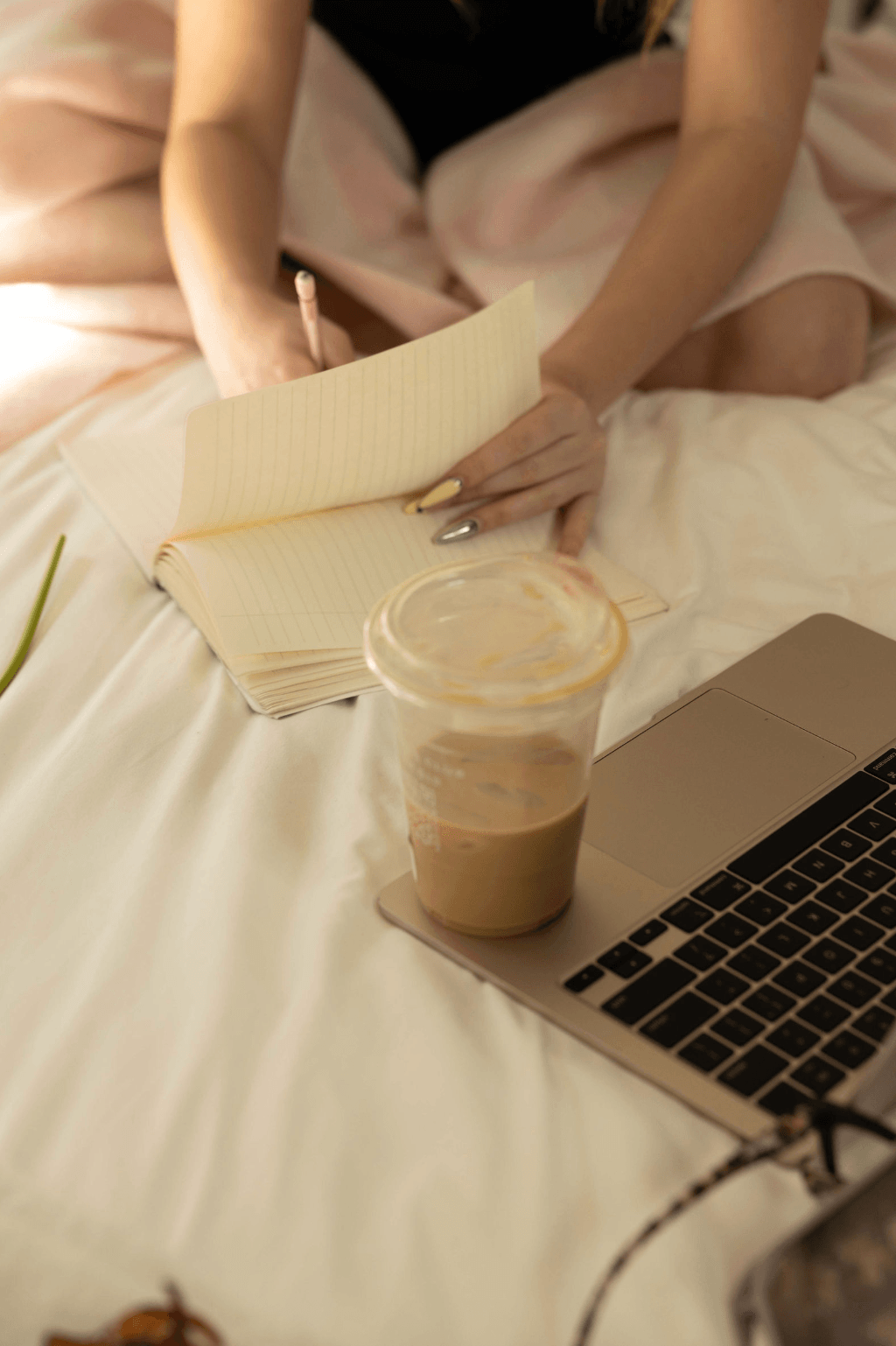 Tess flipping through a journal in bed, iced coffee and open laptop nearby — the intentional morning routine that inspired Callah.