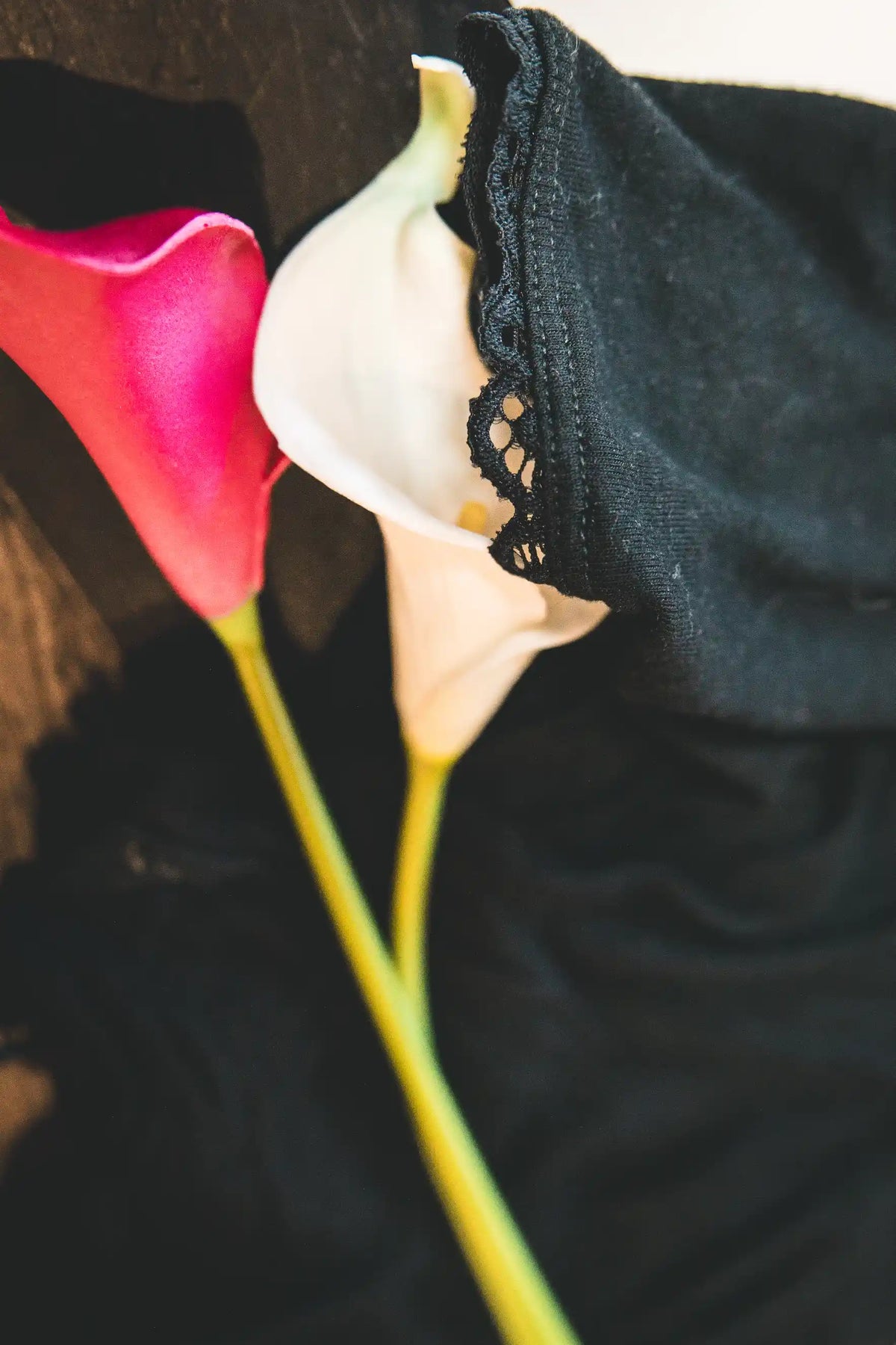 Close-up of Callah Cami in Black with lace trim detail, styled 
with pink and white calla lilies